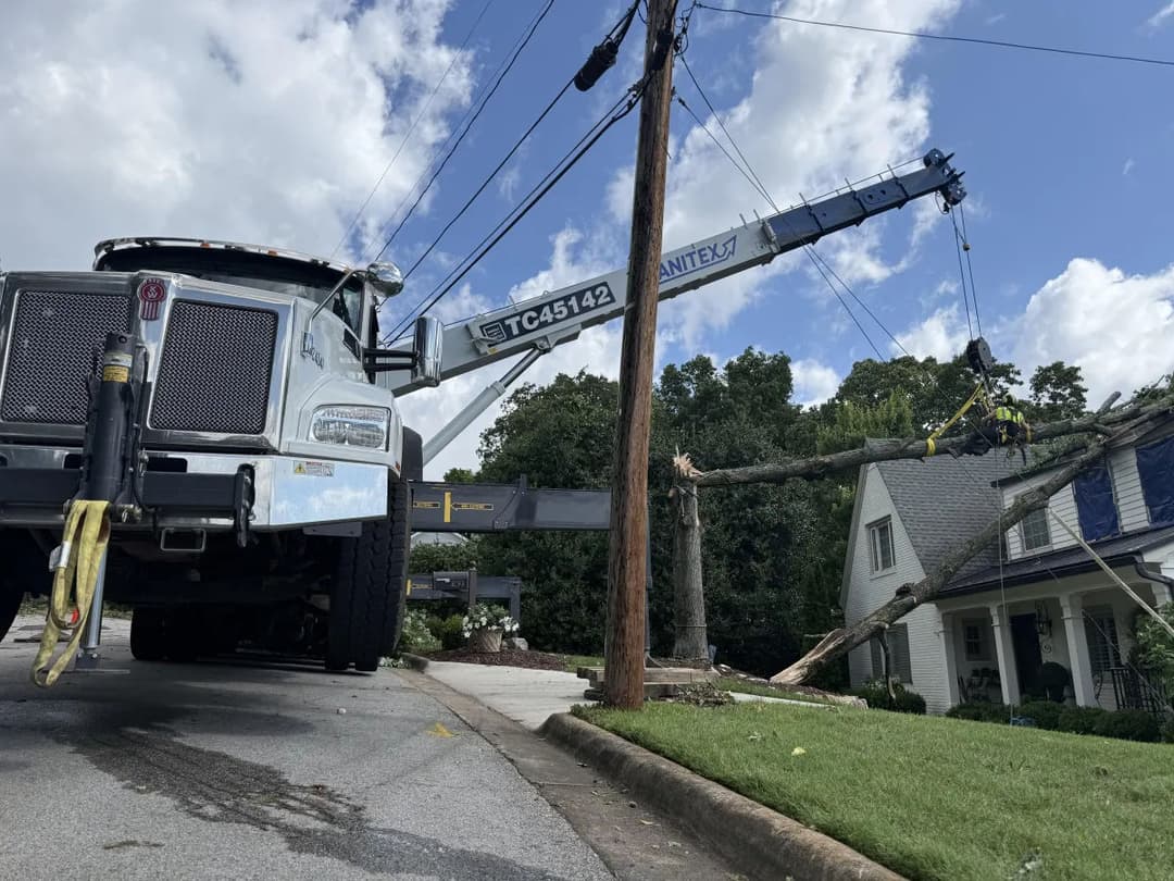 Tree removal operation with crane near a damaged house and fallen power lines.