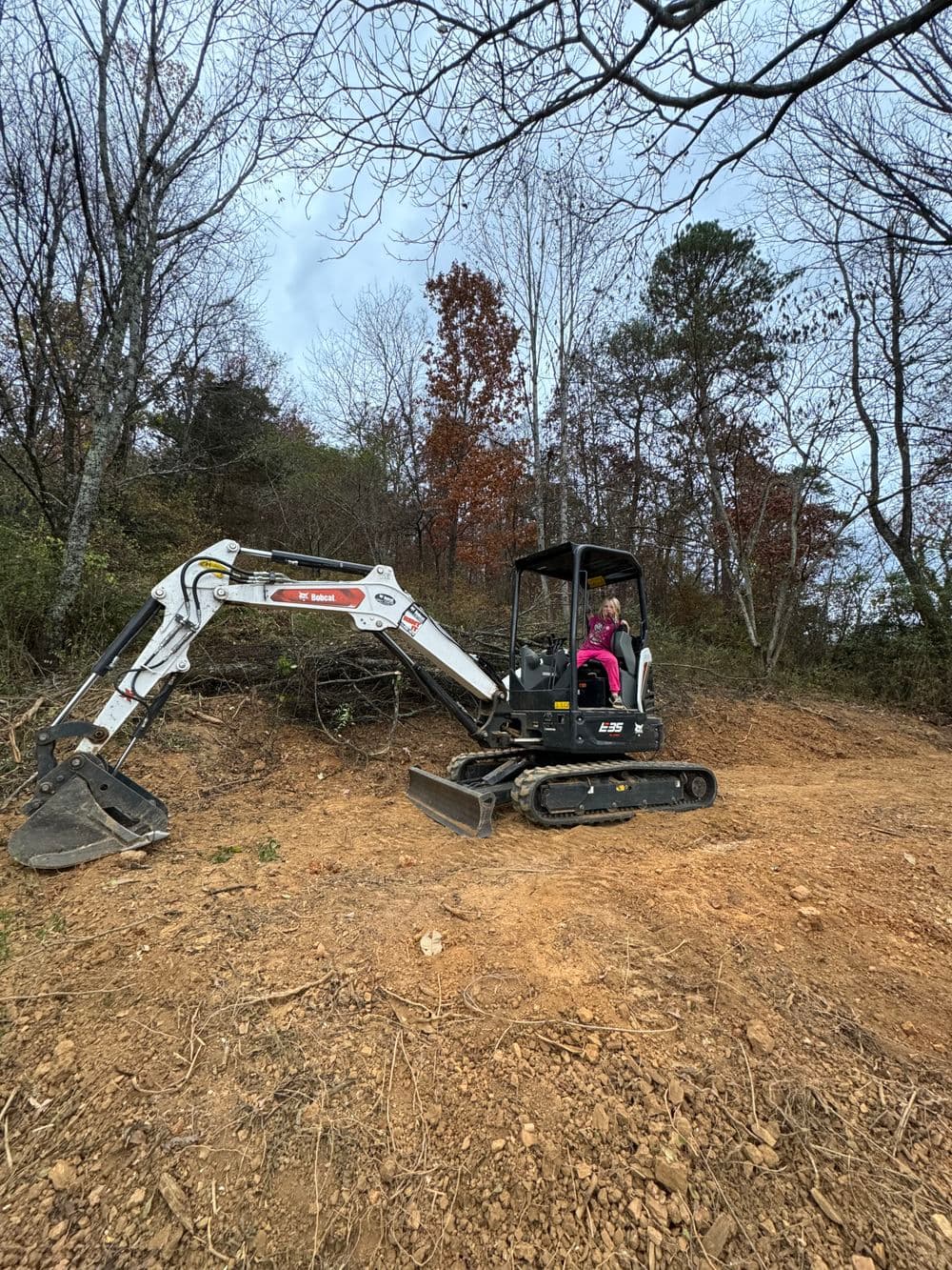 Excavator in action on a rural landscape with trees and autumn foliage.