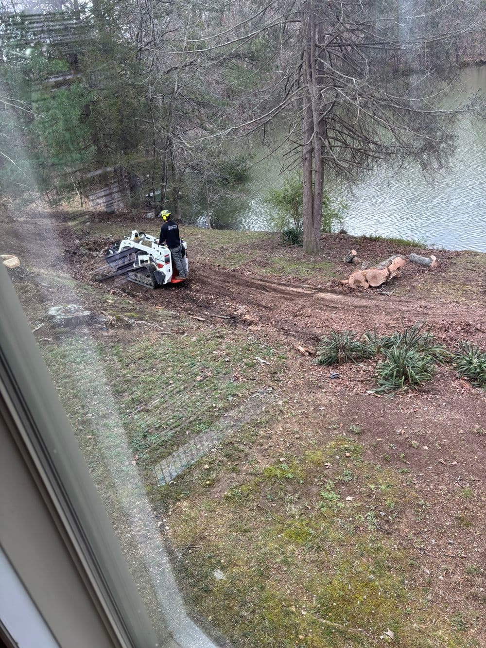 Construction worker operating a skid steer loader near a water feature in a residential area.
