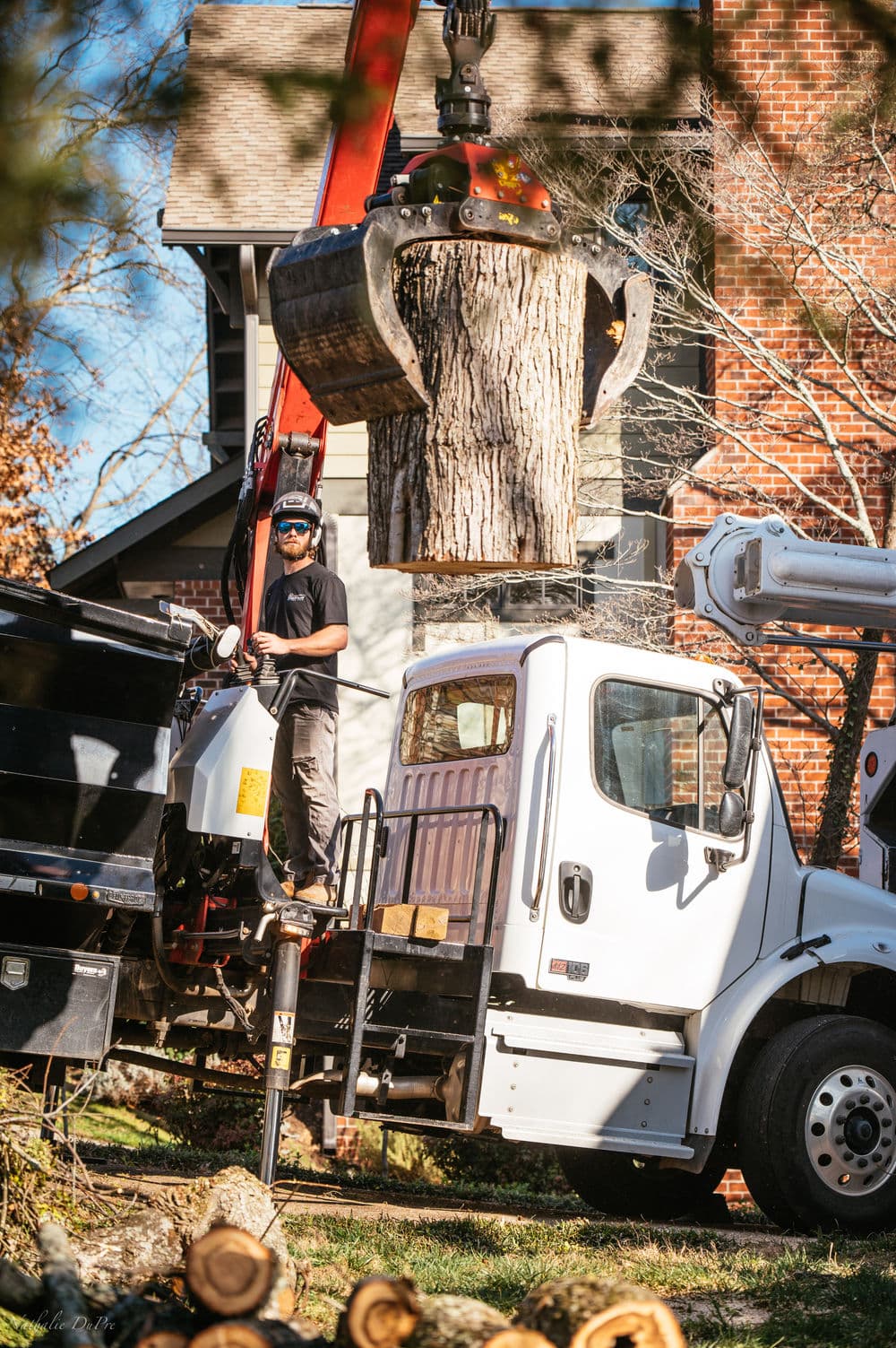 Tree removal service using a crane to lift a large log from a residential property.